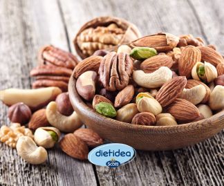 Ciotola colma di frutta secca a guscio assortita, tra cui noci, mandorle, anacardi e pistacchi, appoggiata su un tavolo in legno con logo Dietidea Riso Scotti in basso al centro.