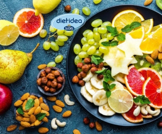 Piatto colorato con frutta fresca di stagione (arance, kiwi, uva, banana, limone, pera) e frutta secca assortita (mandorle, nocciole, anacardi)
