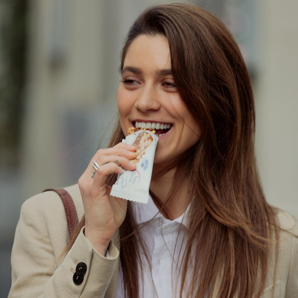 Ragazza che mangia una barretta Dietidea sorridendo mentre cammina per strada, mostrando la praticità e il gusto dello snack in qualsiasi momento del giorno. 